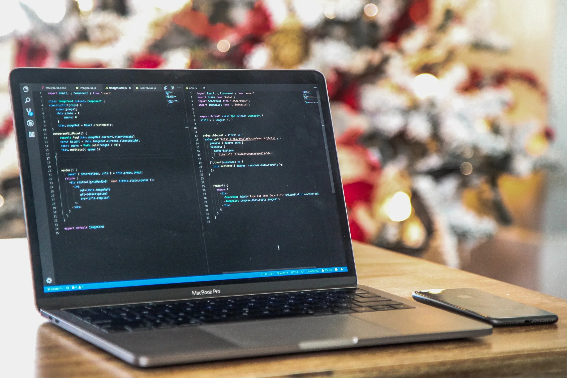 A laptop showing code in an editor on a wooden table, with a decorated holiday tree blurred in the background.