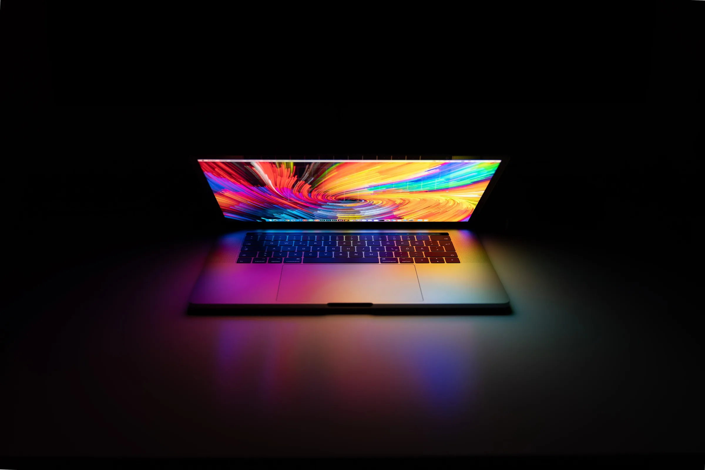 A half-open laptop glowing with a colorful swirl on its screen in a dark room.