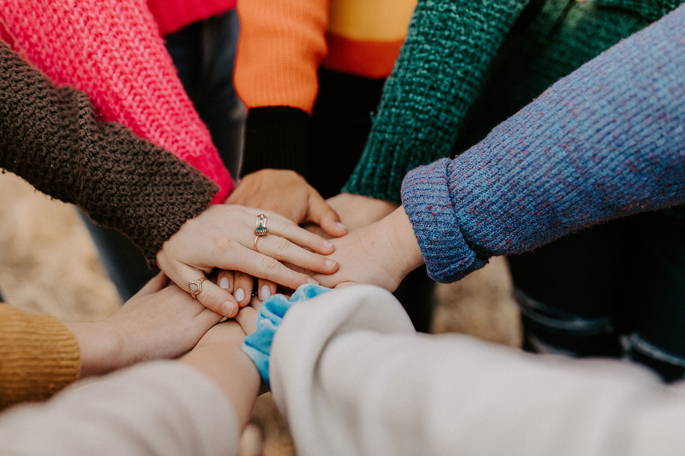 A group of people in colorful sweaters stacking their hands together in a circle.